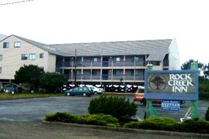 Outside of the Rock Creek Inn, beige building with long outdoor corridors, parking lot and sign